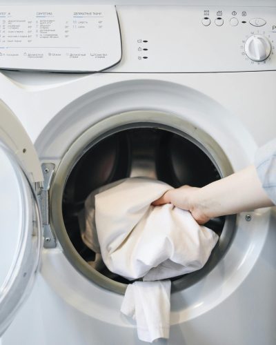 pexels photo 4440652 4440652 Close-up of a person's hand putting laundry into a front-loading washing machine.